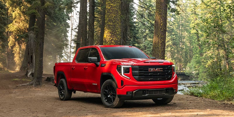 Red GMC Sierra 1500 parked on a dirt path in a forest